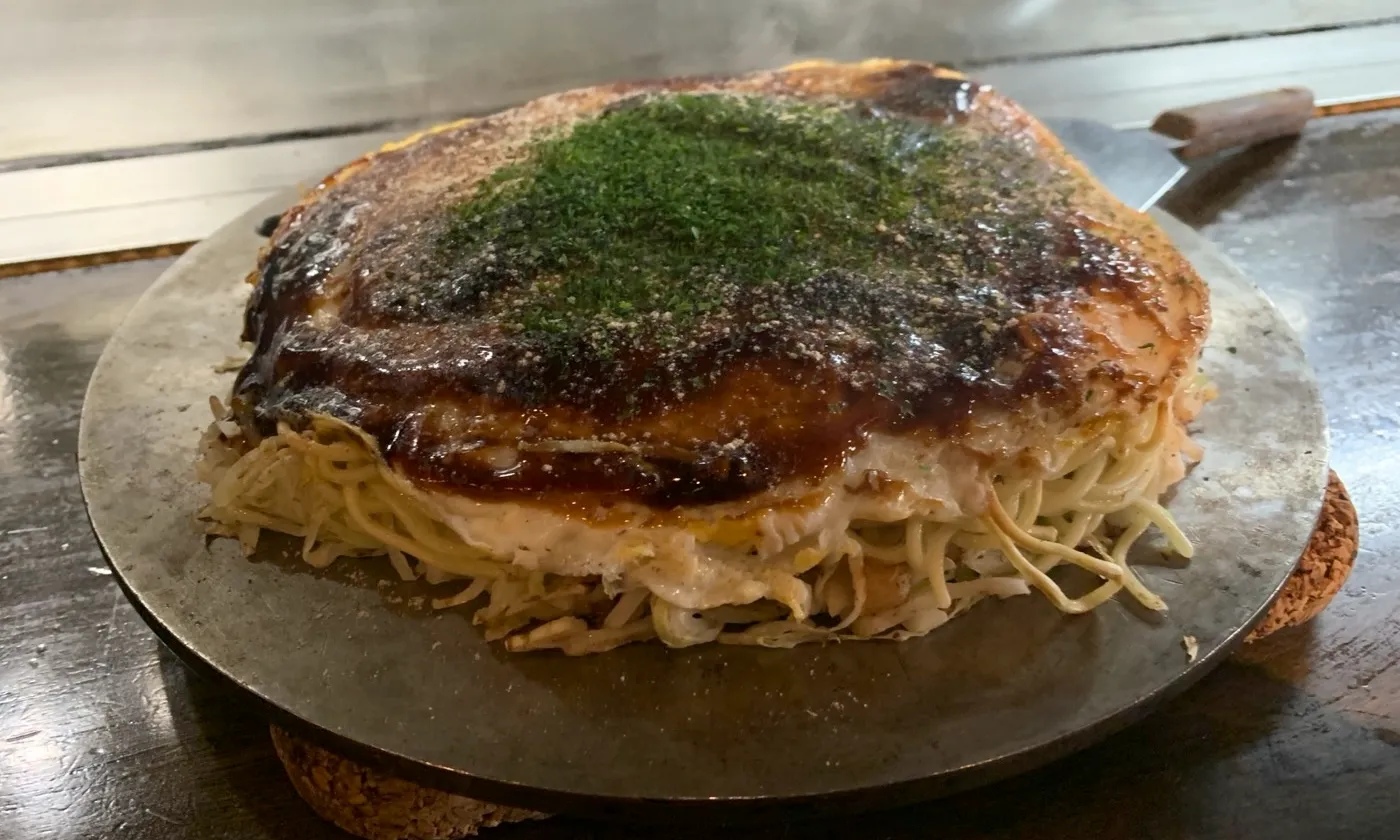 Hiroshima-style okonomiyaki cooking on a hot griddle